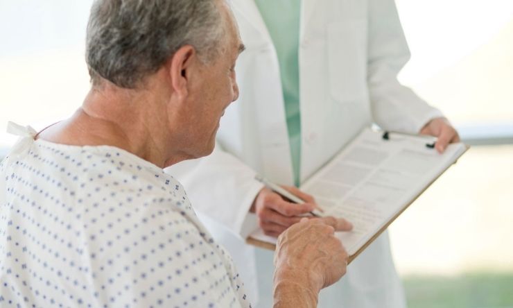 Male patient in hospital bed signing document