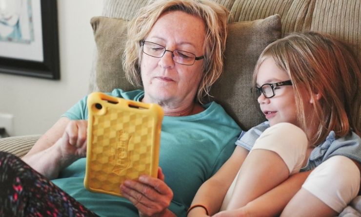 Middle aged woman sitting on couch with granddaughter reading