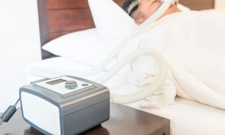 Image of person in background asleep in bed with breathing machine