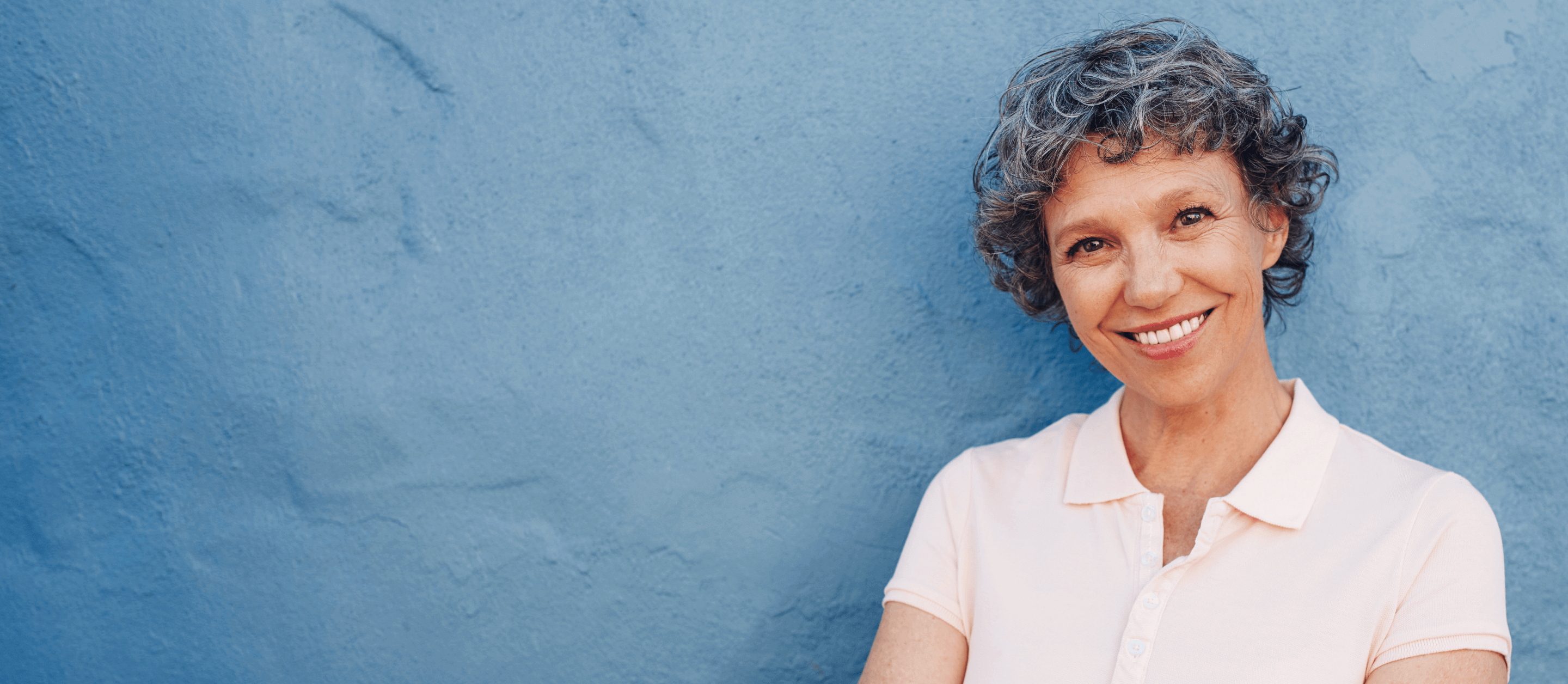 A woman leaning against a wall smiling at the camera