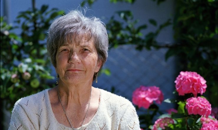 Older woman sitting in garden with pink flowers in background