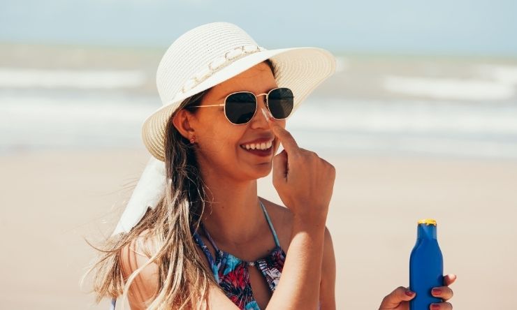 Lady at beach wearing sunglasses, hat and sunscreen