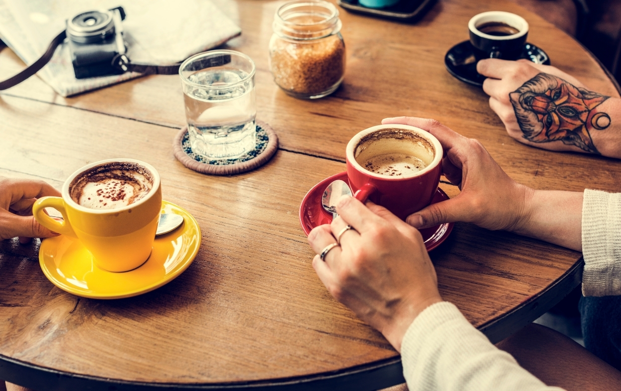 hands holding coffee cups around table in cafe