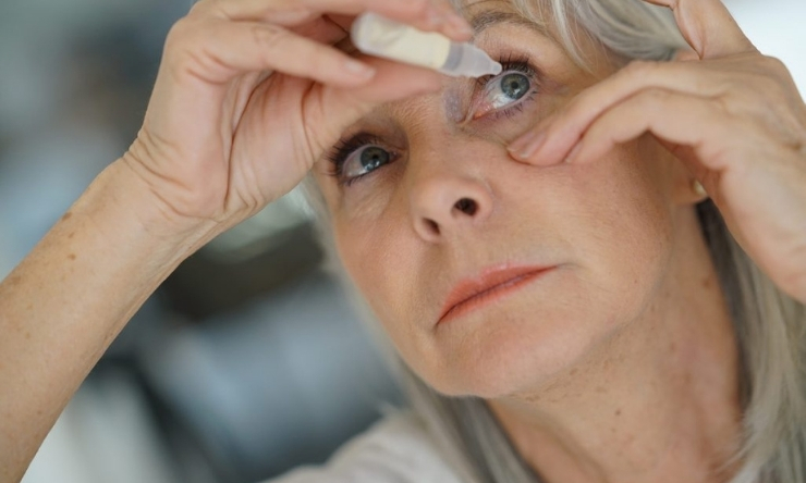 Image of middle aged blonde haired woman applying eye drops to her eyes