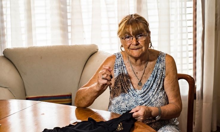Image of older woman sitting at dining table sewing fabric