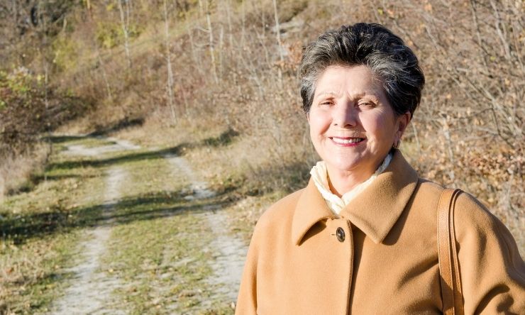 Image of older woman standing with unsealed country road in background