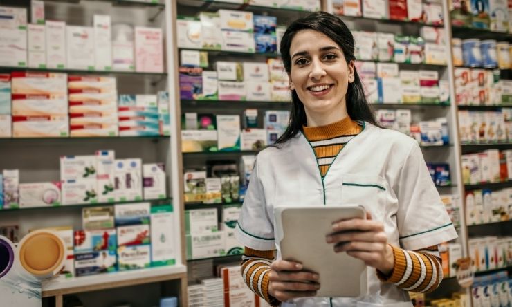 Image of smiling pharmacist standing in front of shelves with medication 