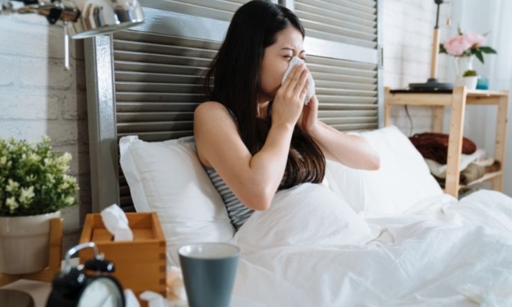 Image of woman sitting up in bed at home blowing her nose