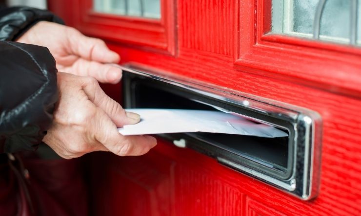 Image of mail being placed in mailbox through a red front door
