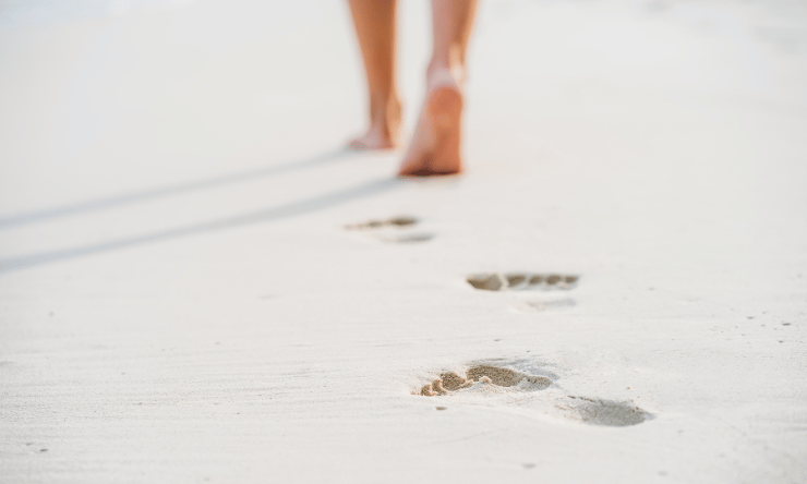 A person walking on a beach leaving footsteps in the sand.
