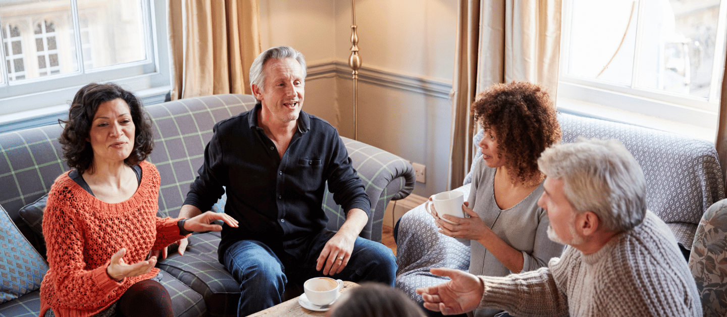 A group of 4 adults in a sunny lounge room talking happily