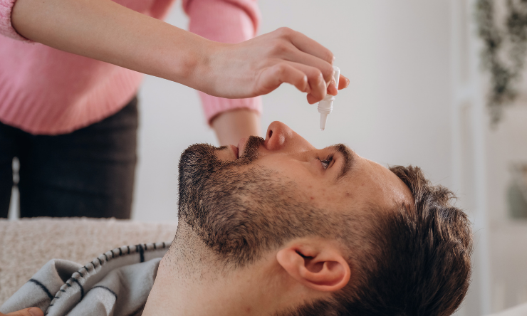 Lady putting eye drops into mans eyes