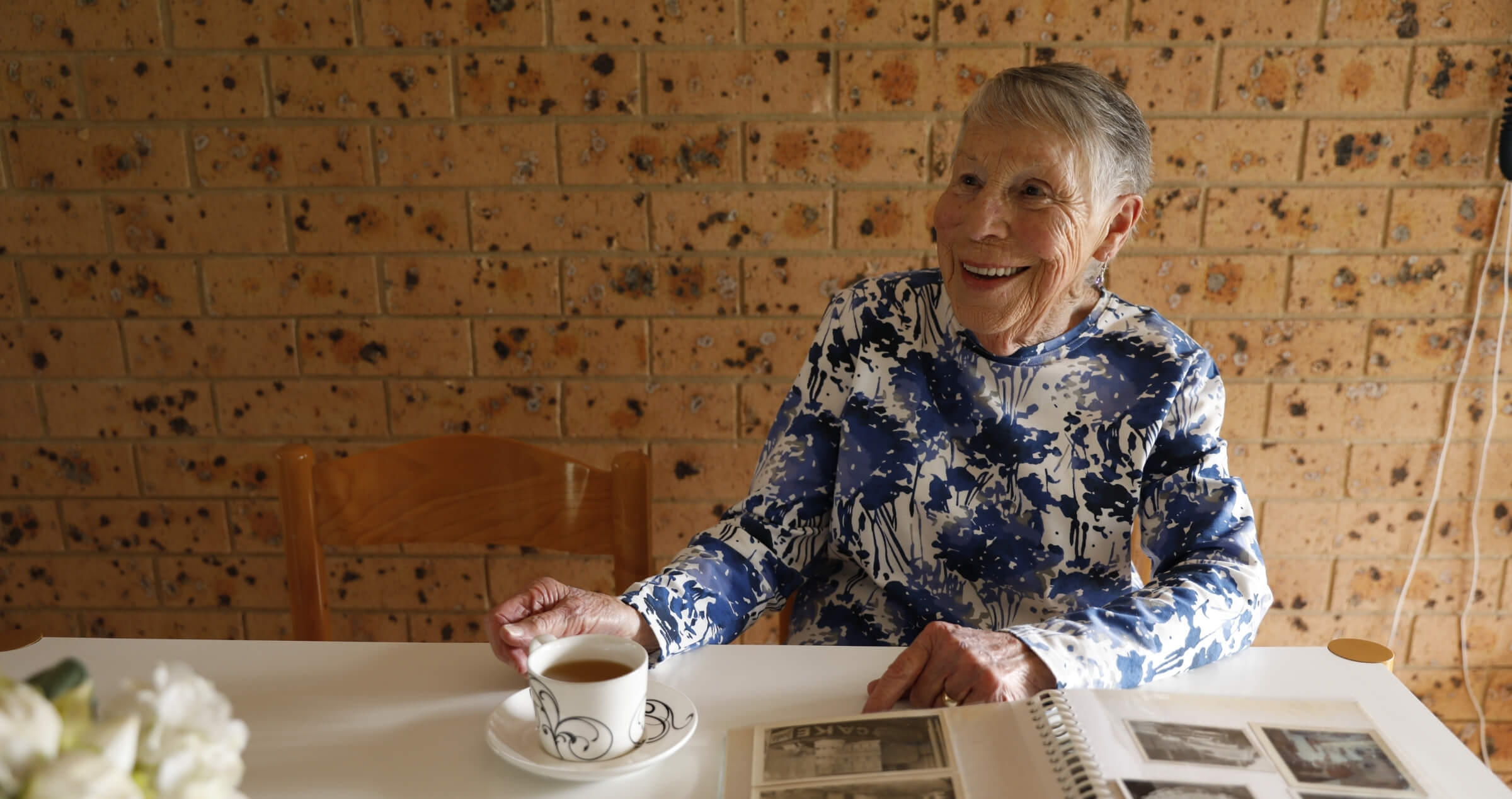 Image of older woman sitting at table drinking cup of tea and looking through photo album