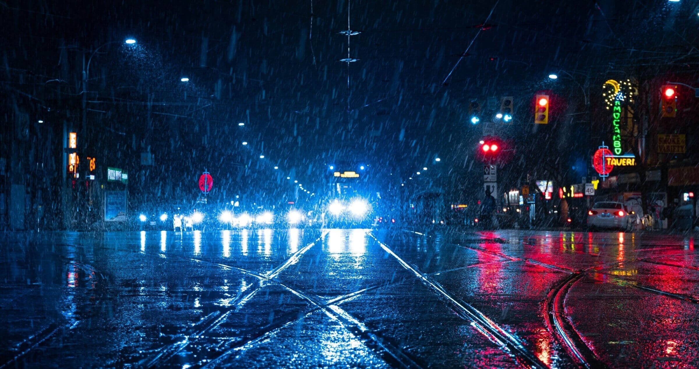 A busy city intersection on a dark and raining night with lights reflecting off the road