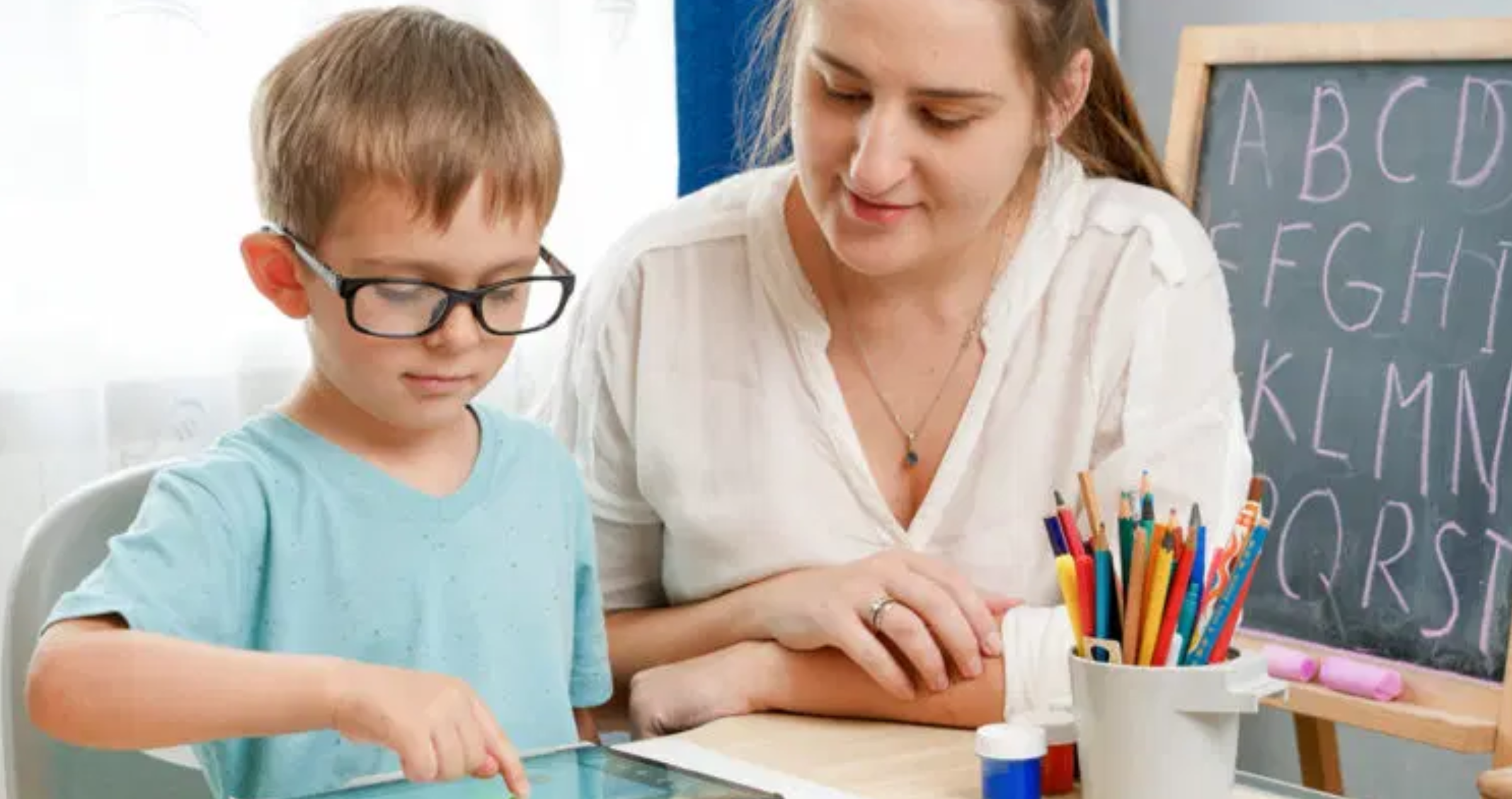 Image of a child (wearing glasses) using an ipad with his teacher