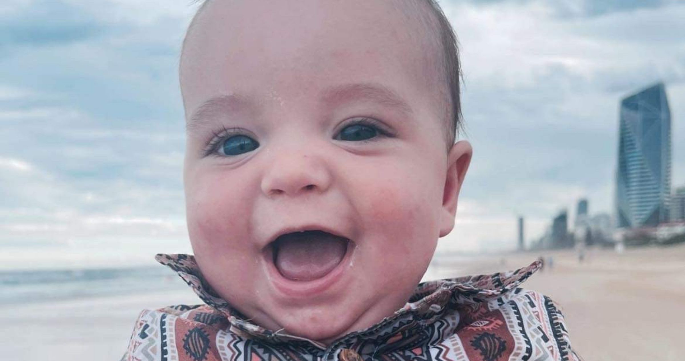 Image of smiling baby boy with beach in background