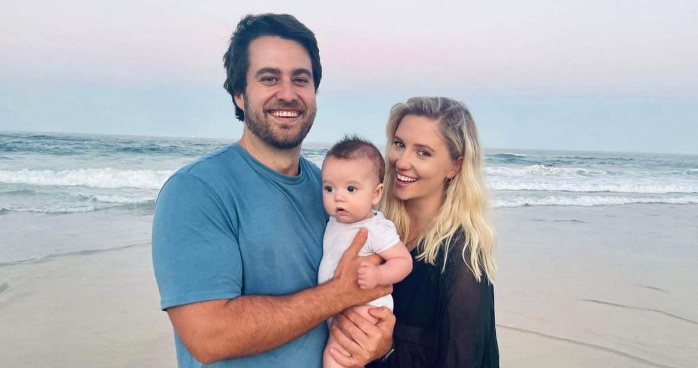 Image of young family with father, mother and baby boy, standing on beach