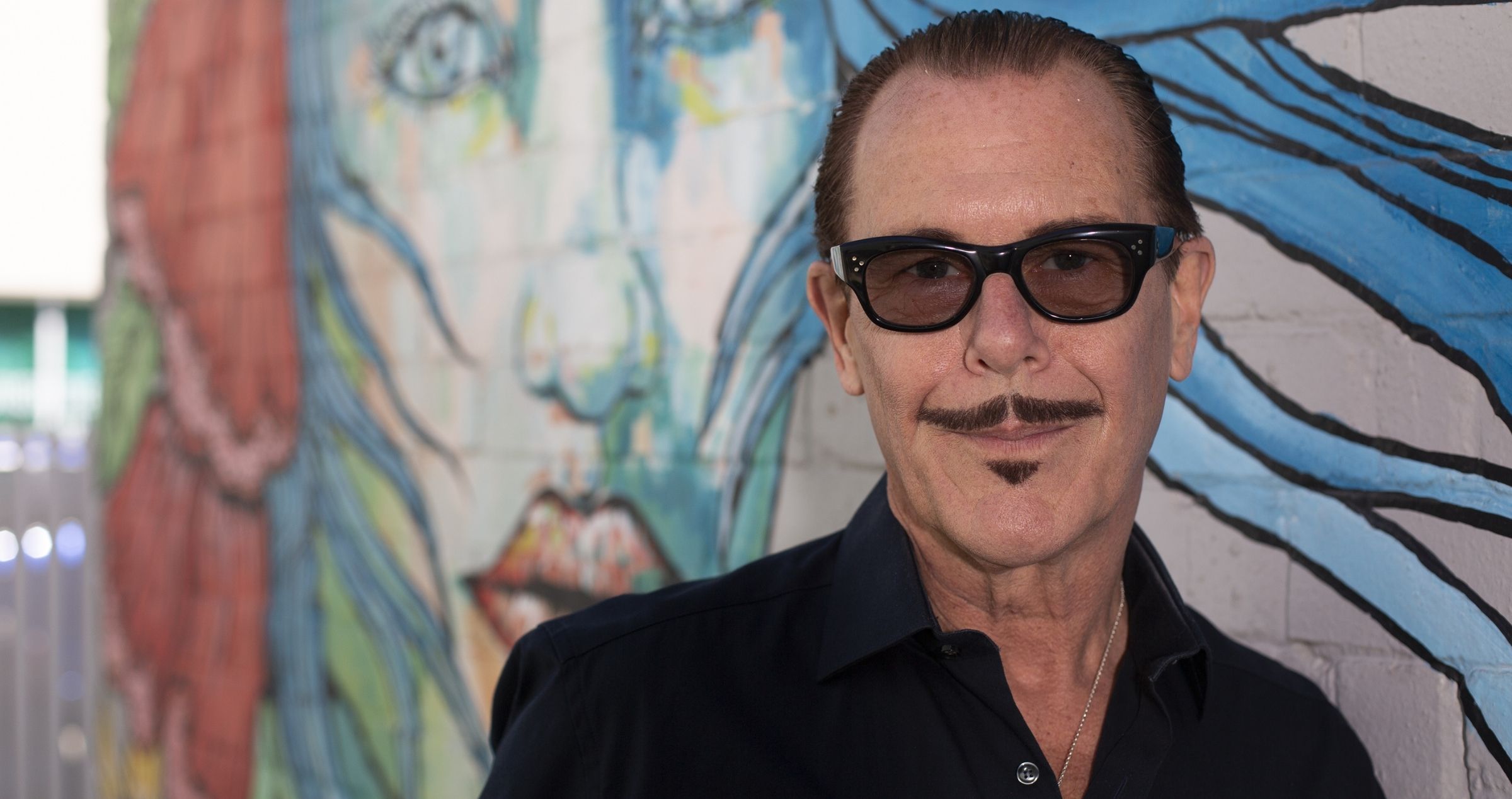 Kirk Pengilly leaning against wall with grafitti