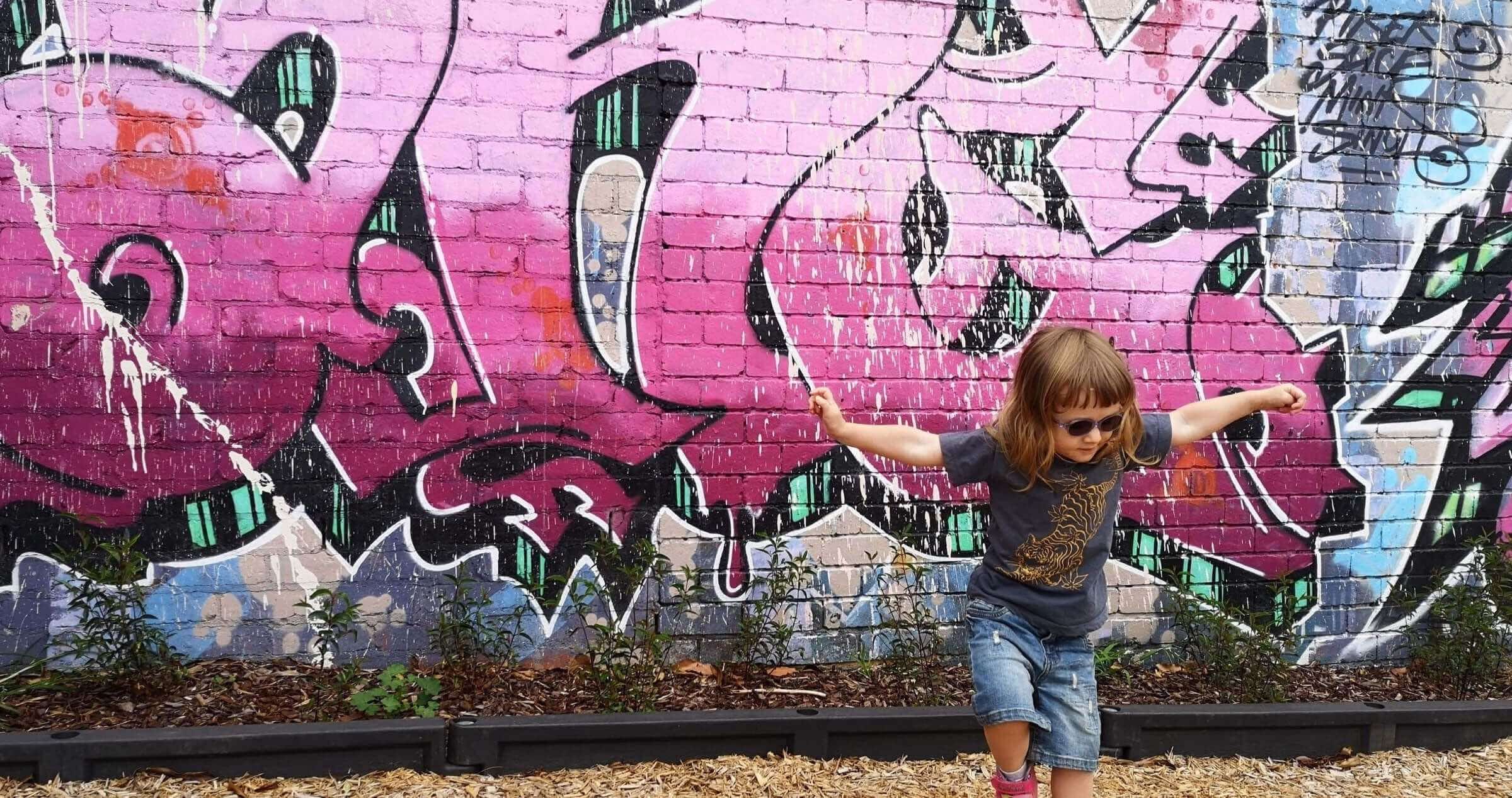Image of young girl dancing in front of bright pink graffitied wall