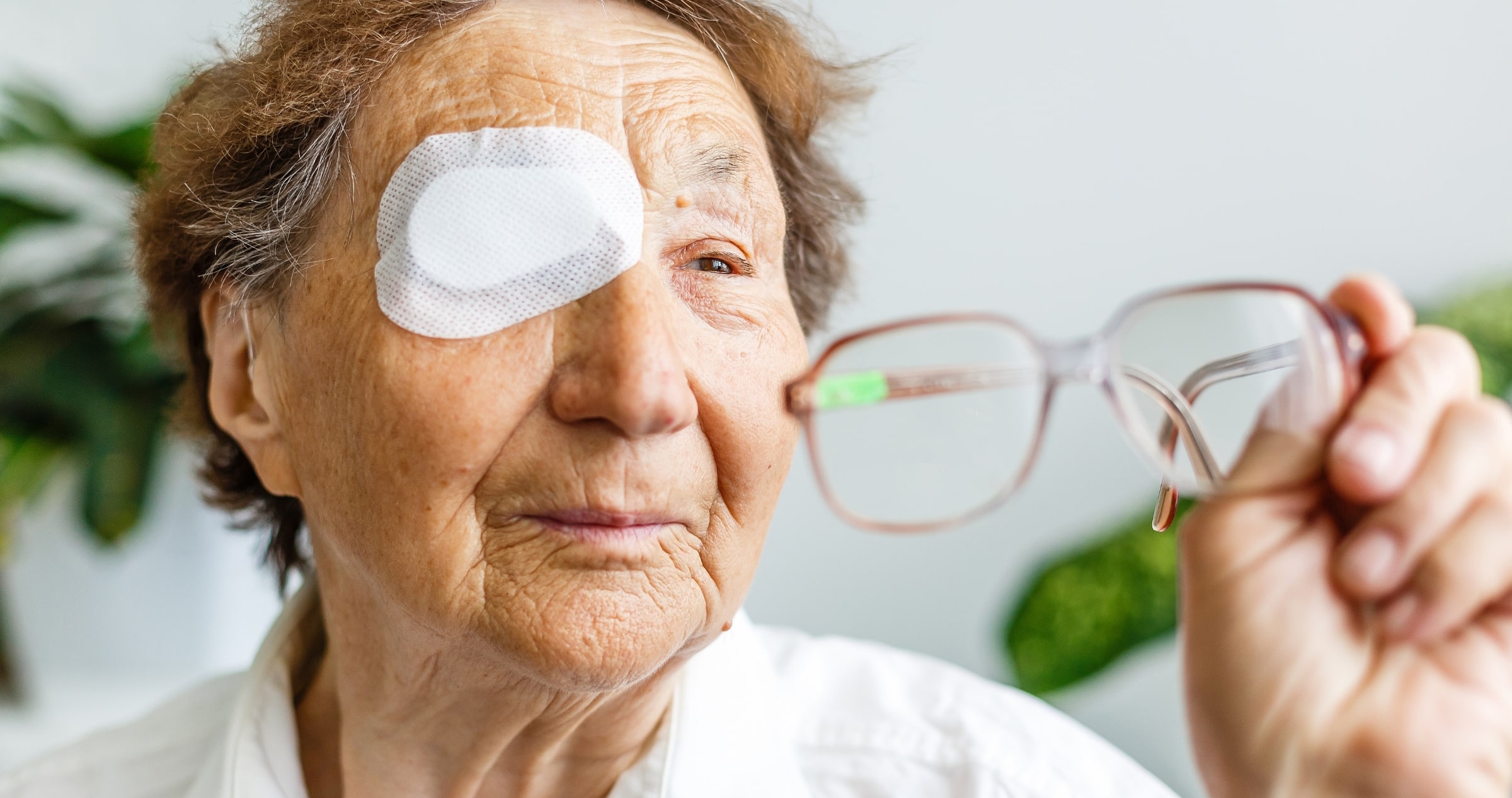 Image of older woman with post surgery eye patch, holding up her reading glasses