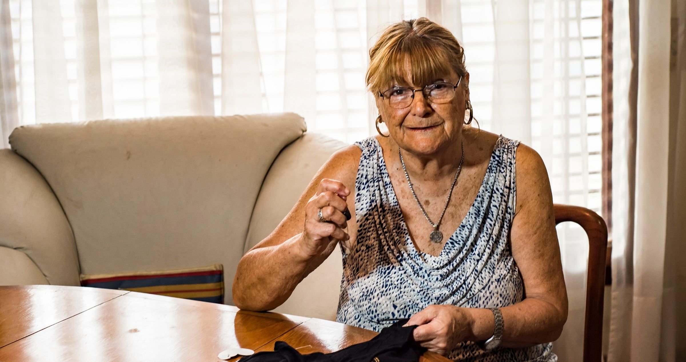 Image of older woman sitting at dining table sewing fabric
