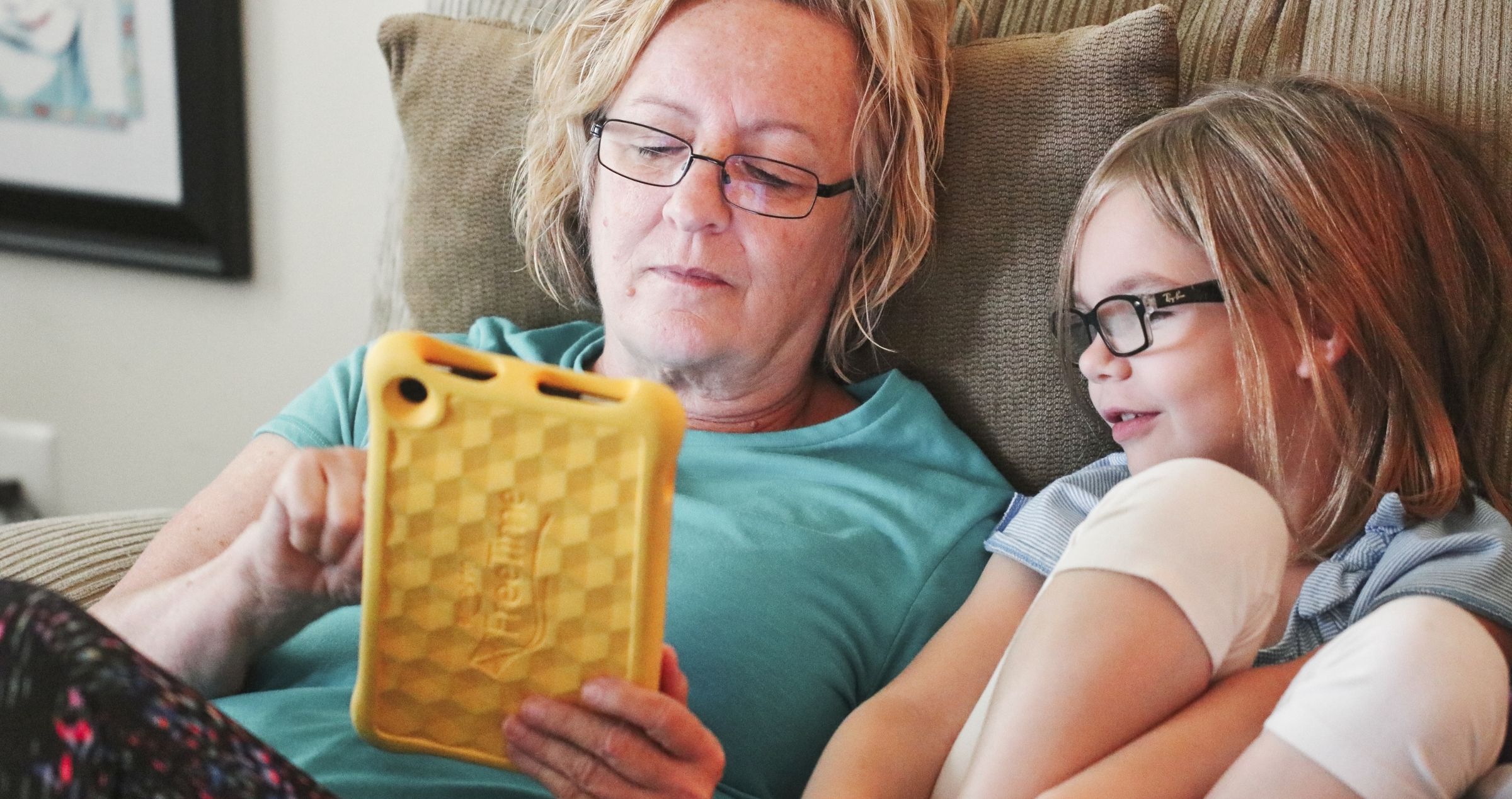 Middle aged woman sitting on couch with granddaughter reading