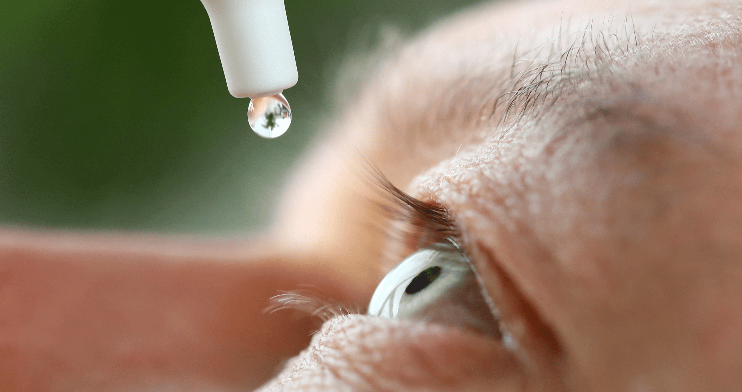 A close up of an eye drop about to be instilled into a man's eye.