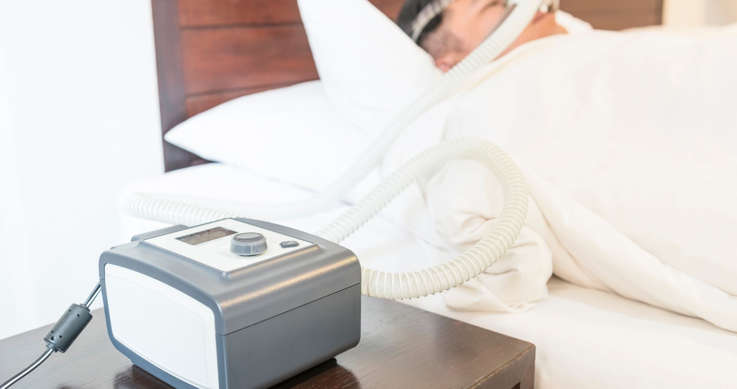 Image of person in background asleep in bed with breathing machine