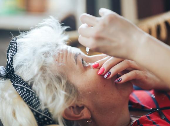 Woman with grey hair instilling glaucoma eye drops at home