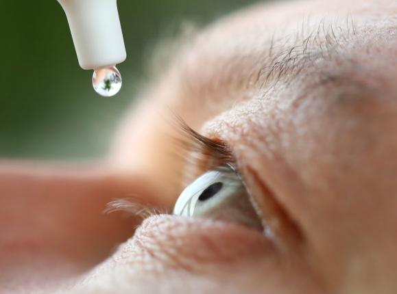 Close-up of a mans eye with an eye drop about to be instilled from above