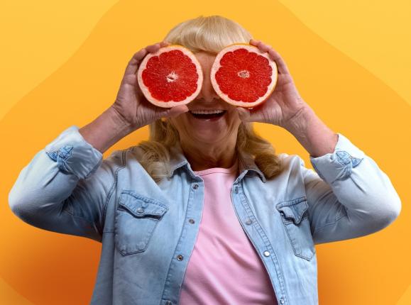 Woman in denim jacket and pink t shirt holding up grapefruit halves over her eyes