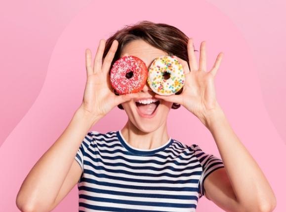 Young woman holding up doughnuts over her eyes and smiling