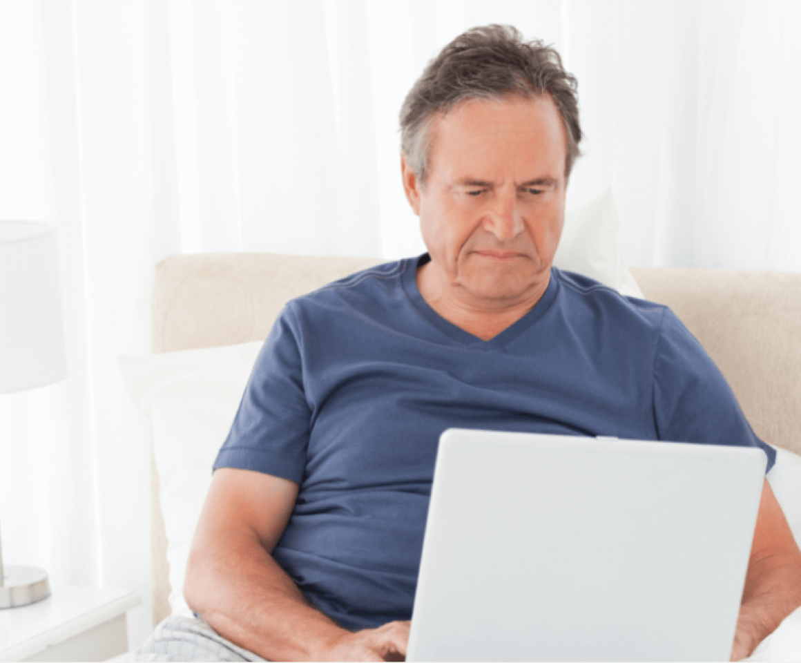 Middle aged man sitting in bed searching on his laptop