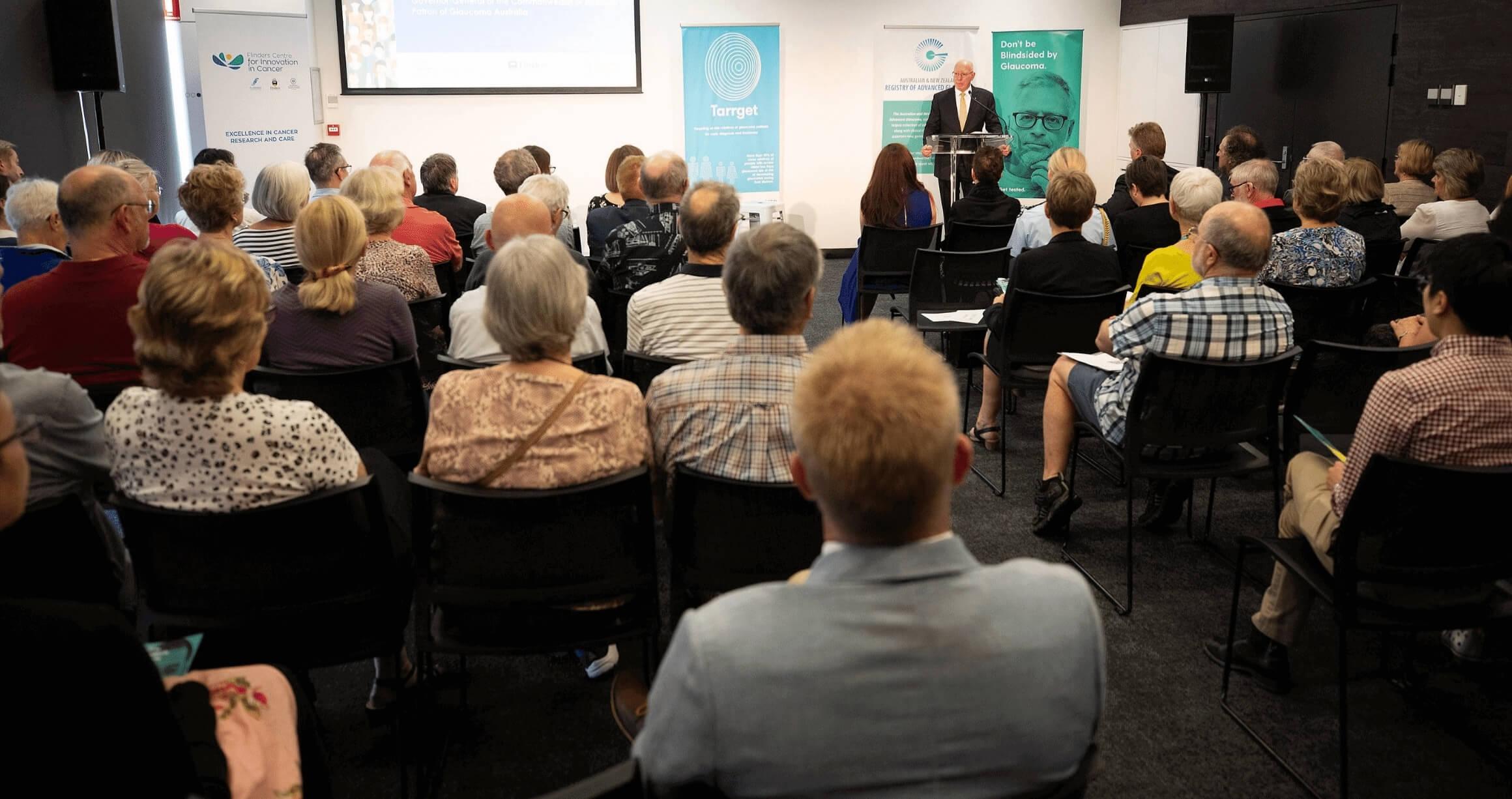 image from rear perspective of audience in a conference room listening to the Governor General of Australia explain the importance of glaucoma awareness